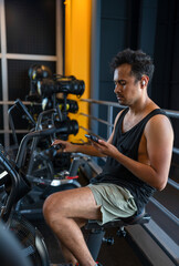 Fototapeta na wymiar Young man cheking his phone while he is on a cycling machine in the gym