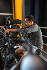 Young man training hardly on cycling machine in the gym