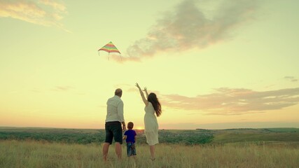 Family with son play together in the park in summer, fly a kite into the sky. Family happiness. Mom, child, dad travel. Kid plays with parents outdoors, childhood dreams. Family love concept