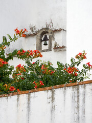 Portugal, Obidos. Orange trumpet vine growing below a church bell in the medieval village of Obidos.