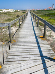 Fototapeta premium Portugal, Costa Nova. Beach and board walk at Costa Nova beach resort with the clock and bell tower of Our Lady of Health Church in the distance near Aveiro.