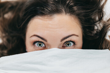 Frightened shocked woman with big eyes lies under blanket in bed and realizes she overslept, did not hear alarm, missed important meeting. 