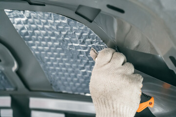 Worker glues soundproofing material to inside of car hood. Process of car sound insulation...