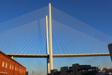 View of the bridge against the blue sky. The cables and high pylons of this long cable-stayed road bridge. Steel and concrete materials for this transport structure. Largest suspension bridge Crossing