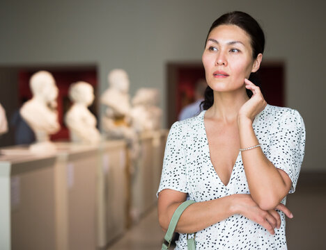 Thoughtful adult woman watching sculptures in museum hall