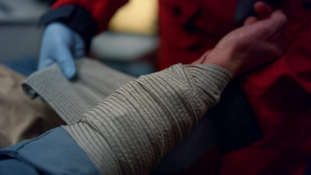 Closeup ambulance paramedic in gloves wrapping patient hand with elastic bandage