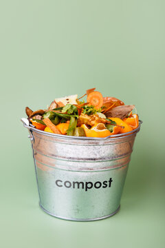 Sorted kitchen waste in compost-bucket on green background. Compost-container top view. Sustainable lifestyle. Vegetable, fruit peels, scraps from food preparation collected in trash-can for recycling