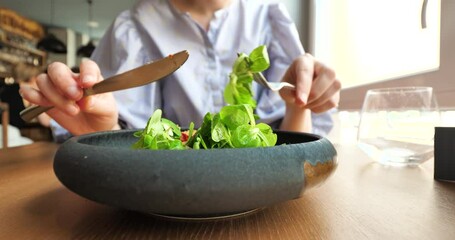 Front view of woman eating delicious bio organic vegan green salad in luxury restaurant from rustic plate