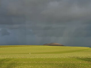 Einsamer Berg auf dem Feld mit Sonnenstrahlen auf dunklem Wolkenhimmel im Winter