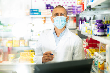 Caucasian male pharmacist in lab coat and face mask standing at counter in chemists shop and writing recipe.