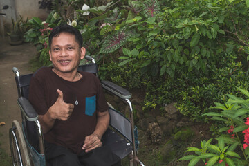 A paraplegic middle aged man in his wheelchair gives a thumbs up sign in approval while outside his...