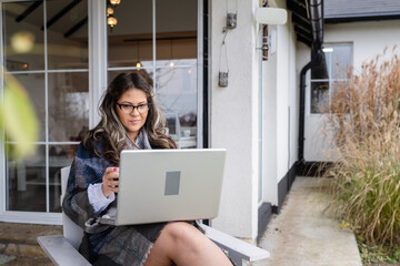 One young adult caucasian woman sitting in front of her home in day holding laptop computer working or using for social network while having a cup of coffee happy smiling real people copy space