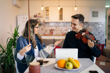 Young adult caucasian man student learning to play violin with help of his professor woman female mentor teaching him how to improve skill at home explaining lesson real people private class concept