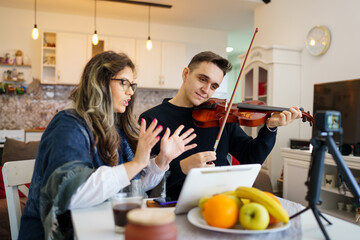 Young adult caucasian man student learning to play violin with help of his professor woman female mentor teaching him how to improve skill at home explaining lesson real people private class concept