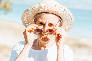 Traveler tourist smiling mature elderly senior lady woman 55 years old wear white shirt and a hat with glasses outdoors portrait. Happy day exploring and doing new habits. Happy elderly