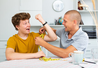 Father using measure tape for measuring girth of his son's biceps