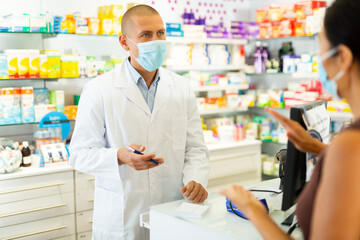 Portrait of pharmacist in medical mask working at the cash register in a pharmacy