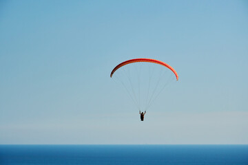 The paraglider hovers high in the sky above the blue sea. Extreme sport backgrounds