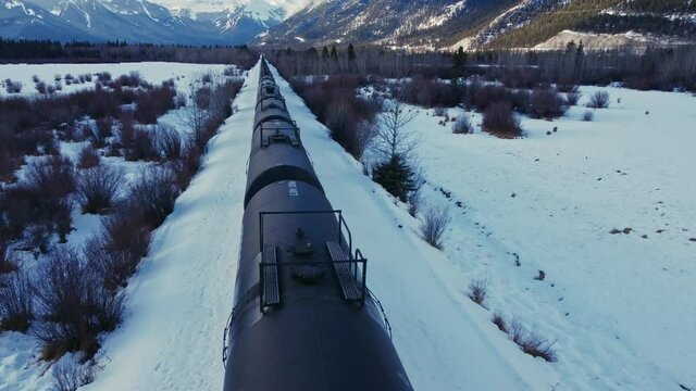 Train in a valley followed in winter snow oil tanks flyover