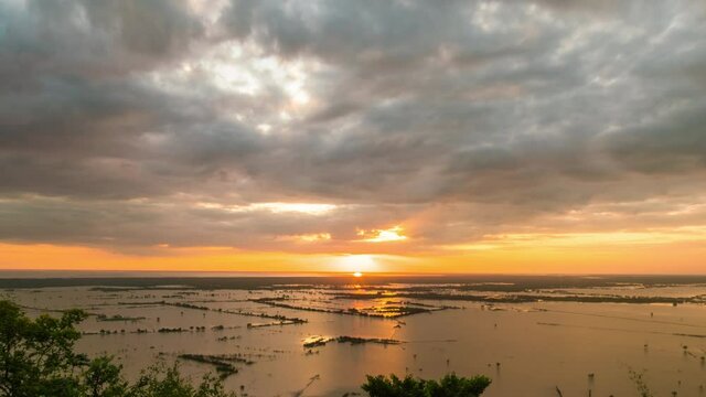 Golden sunset reflection over the horizon of receding Tonle Sap Lake fertile water, revealing sunken paddy fields at the end of rainy season. Dynamic zoom out as the clouds zoom into the scene.