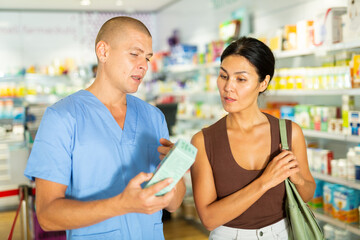 Pharmacist advises customer in a pharmacy, offers medicine for body care