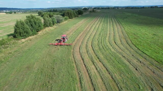 The farmer turns the grass with a hay rake attached to the tractor. Shot from a height.