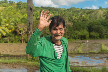A friendly old man waves hi to the camera. A veteran Filipino farmer.