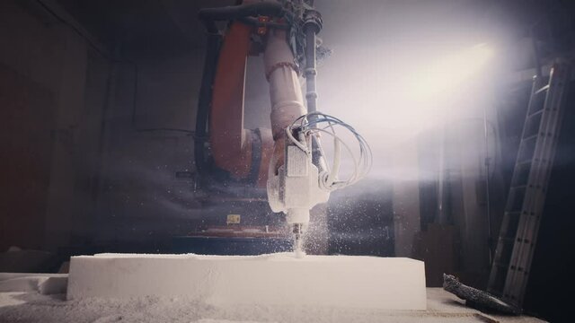 Time lapse of robotic arm milling machine cutting block of polystyrene in cloud of smoke near craftsman in respirator and face shield