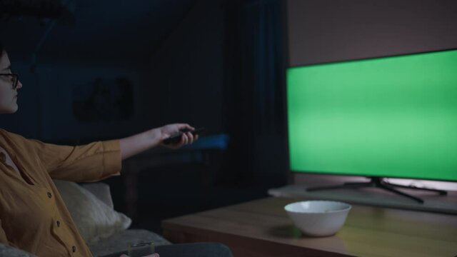 teen girl is sitting on the sofa at home in the evening watching tv and switching channels, chroma key, moving camera
