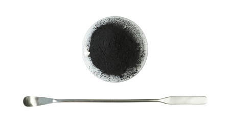 Carbon Charcoal Powder in Chemical Watch Glass placed next to the stainless spatula. Close up...