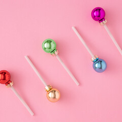 Creative concept with colorful Christmas baubles like a lollipops on a pastel pink background. Minimal New year candy concept