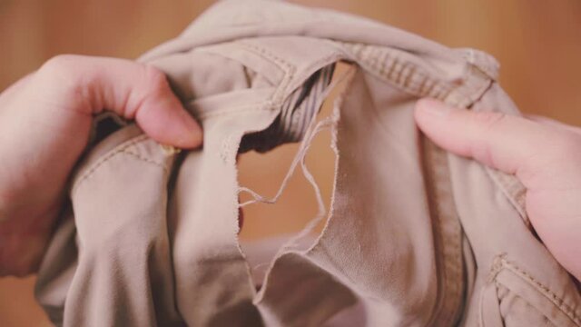 Hands unexpectedly find a large torn hole on the back of beige jeans