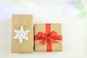 Christmas and New Year background with garland. Gift box wrapped in kraft paper with jute cord. Decorated with a crocheted snowflake. Box with a red ribbon