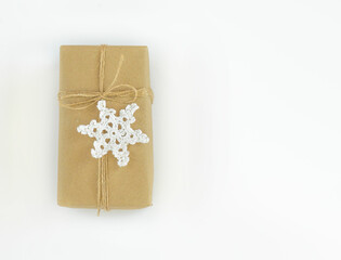 Christmas and New Years flatlay background. Gift box wrapped in kraft paper with jute cord. Decorated with a crocheted snowflake. Place for your text