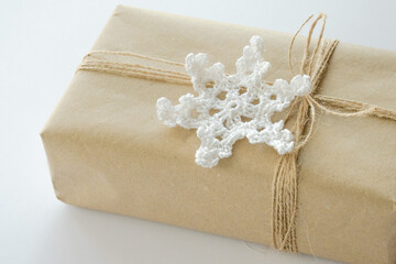 Christmas and New Year background. Gift box wrapped in kraft paper with jute cord. Decorated with a crocheted snowflake