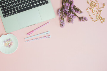 Lavender flower with office items with computer, pens over the pink background. 