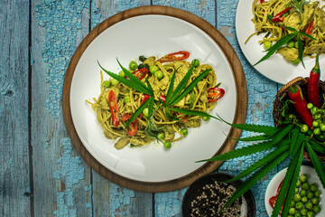 Cannabis spaghetti with chicken green curry sauce  (Thai  style spaghetti khiao waan gai). It sits on the floor of an old blue wooden table. Copy space. Top view.