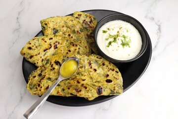 A Food called Methi paratha or Methi thepla is an Indian breakfast dish served with curd and a spoon full of desi ghee. with copy space. Indian fenugreek flatbread. Healthy lunch or dinner.
