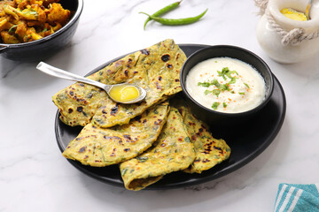 A Food called Methi paratha or Methi thepla is an Indian breakfast dish served with curd and a spoon full of desi ghee. with copy space. Indian fenugreek flatbread. Healthy lunch or dinner.