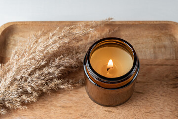 Handmade candle from paraffin and soy wax in glass jar with dry reed grass on wooden tray. Candle...