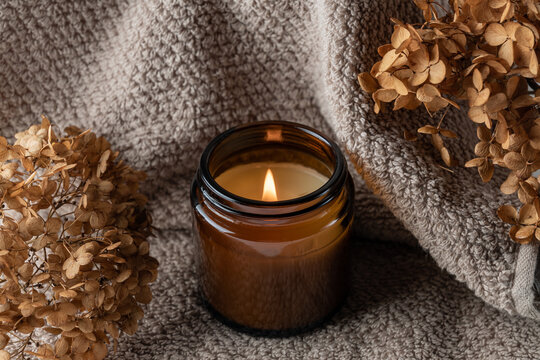 Burning candle in amber glass jar and dry flowers of hydrangea flowers. Cosy lifestyle.