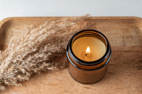 Handmade candle from paraffin and soy wax in glass jar with dry reed grass on wooden tray. Candle making.
