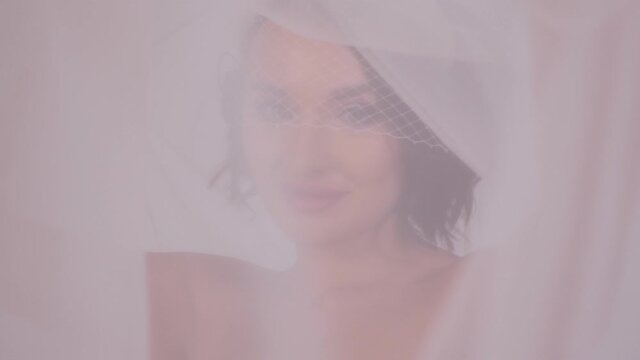 Close-up portrait of a young beautiful bride with dark hair with a head covered with a veil on a white background.