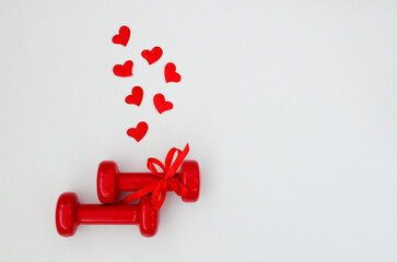 Two red dumbbells and hearts on white background with copy space. Concept of Valentines day, healthy lifestyle, giving gifts, love of sports, shopping