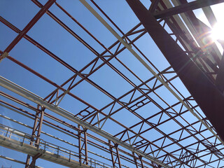 Overhead traveling gantry crane beam, maintenance scaffoldings and truss ceilings of industrial building under construction. Crane runway girder and metal structures against blue sky