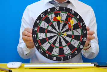 In his workplace, a businessman is holding a dart board and a desk. Workspace with a target and a...