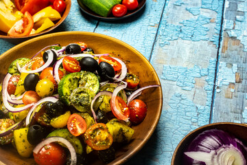 Healthy vegetable salad of fresh tomato, cucumber, onion, black olives,yellow sweet pepper with basil pesto sauce on wooden bowl.Top view, copy space. 