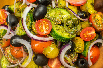 Healthy vegetable salad of fresh tomato, cucumber, onion, black olives,yellow sweet pepper with basil pesto sauce on wooden bowl.Top view, copy space. 