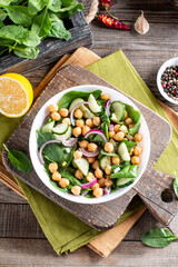 Green vegetable salad with chickpea, spinach, cucumber, red onions, and greens on a wooden table.