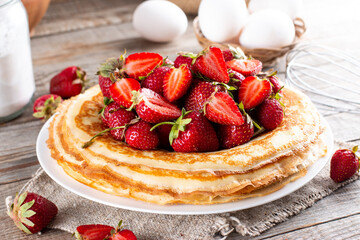 Many pancakes with strawberries. Maslenitsa. A stack of thin freshly baked pancakes with strawberry berries